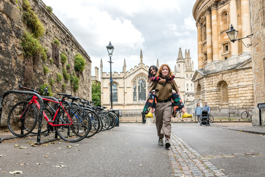 Two Oxford Scholastica students piggy-backing outside the University of Oxford.