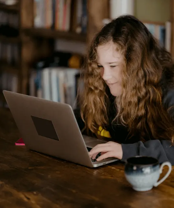 Girl with curly hair sat working at laptop and smiling