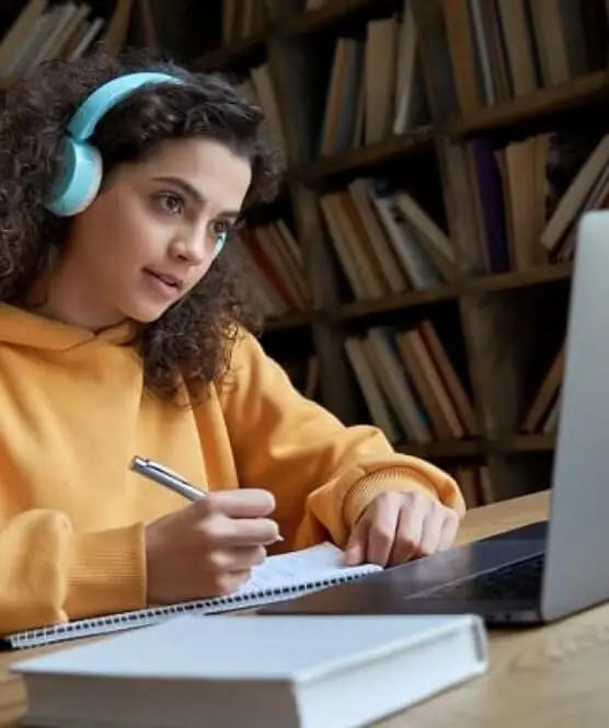 girl in yellow jumper wearing headphones, working in front of a laptop