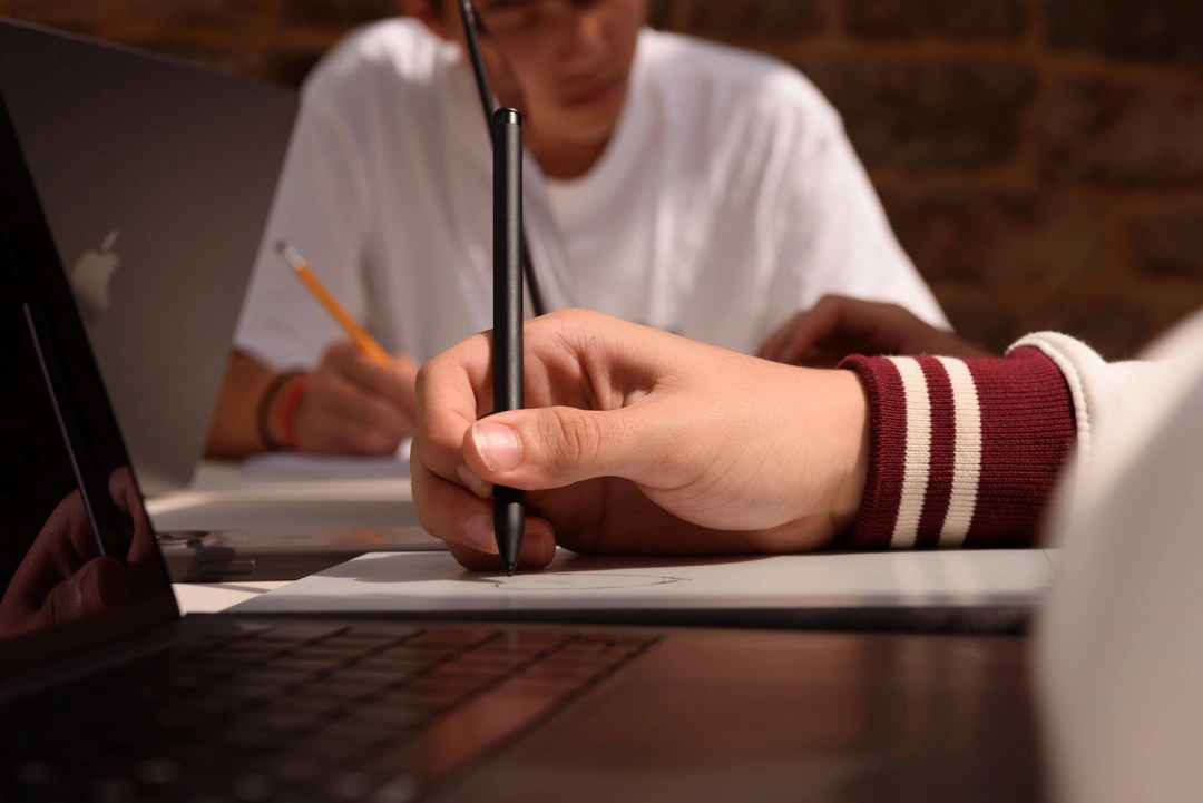 Close up of an OxBright student's hand writing next to a laptop
