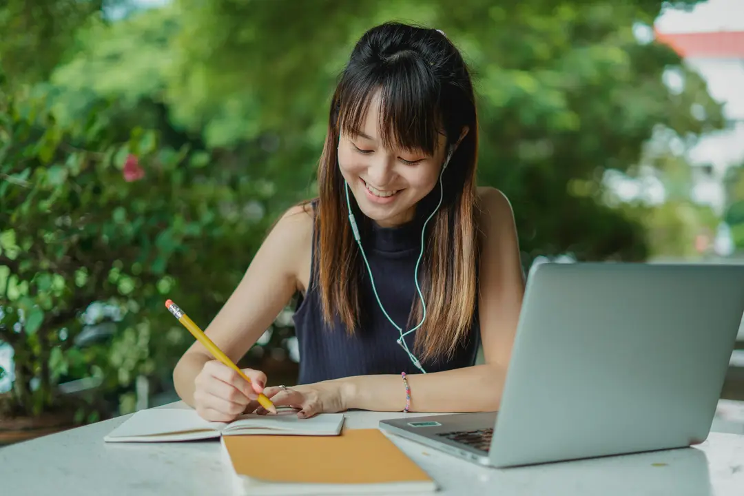 Student smiling while writing in a notebook next to a laptop