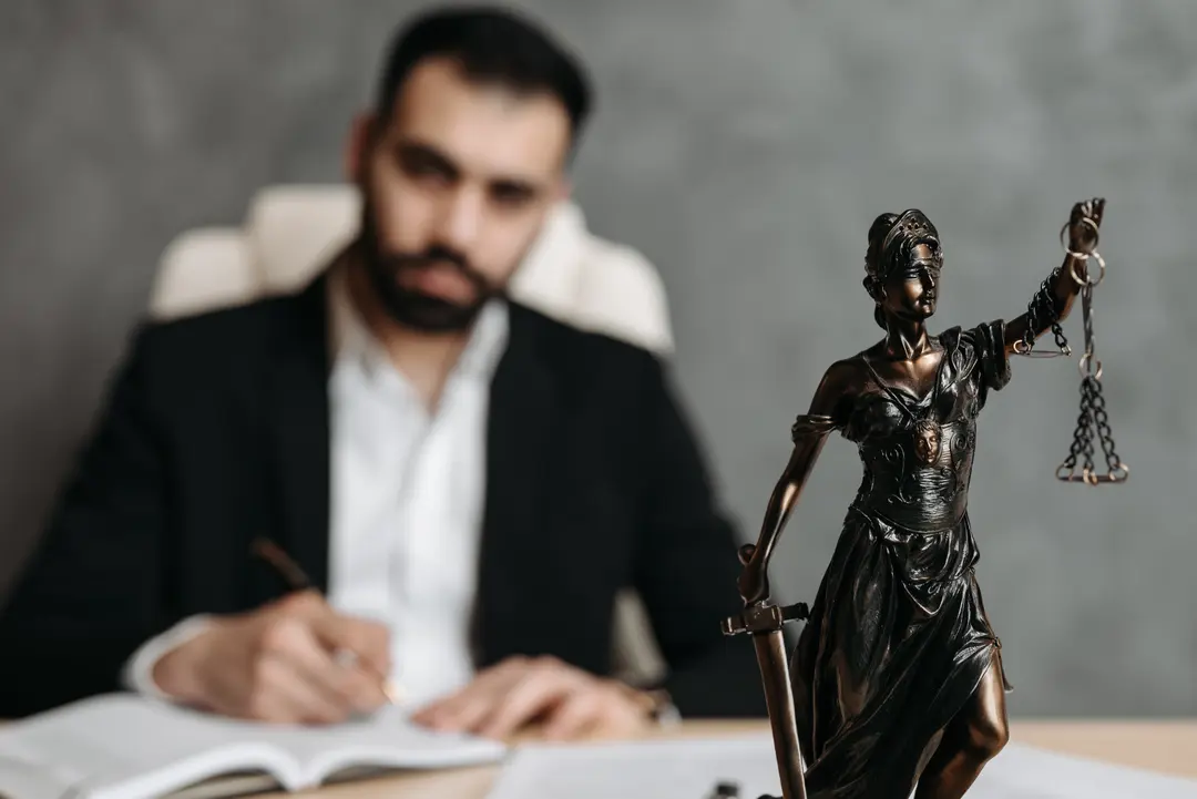 Lawyer writing in the background, with a Lady of Justice statue in the foreground