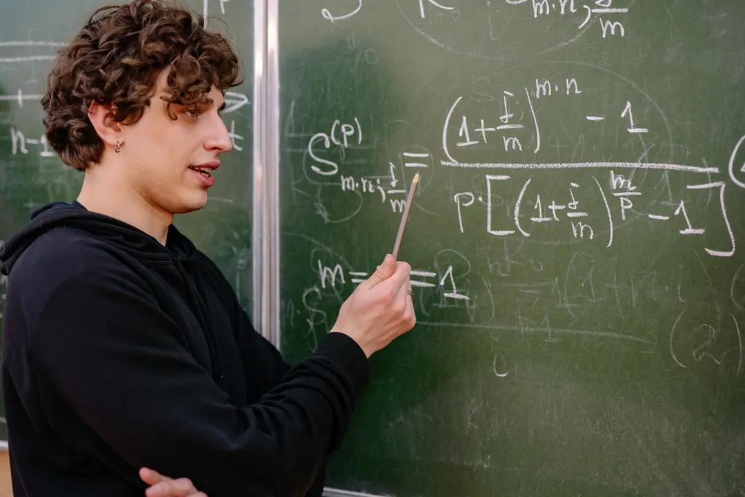 Maths student pointing at a chalkboard with equations on it
