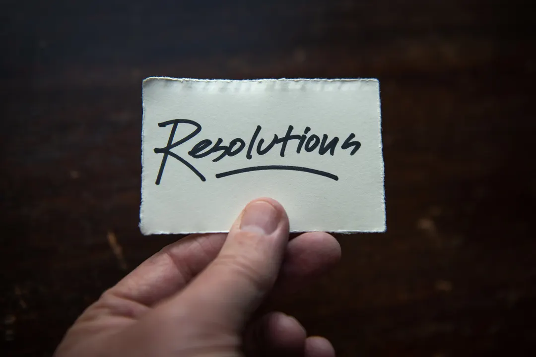 Hand holding a piece of paper, with the word "resolutions" written on it