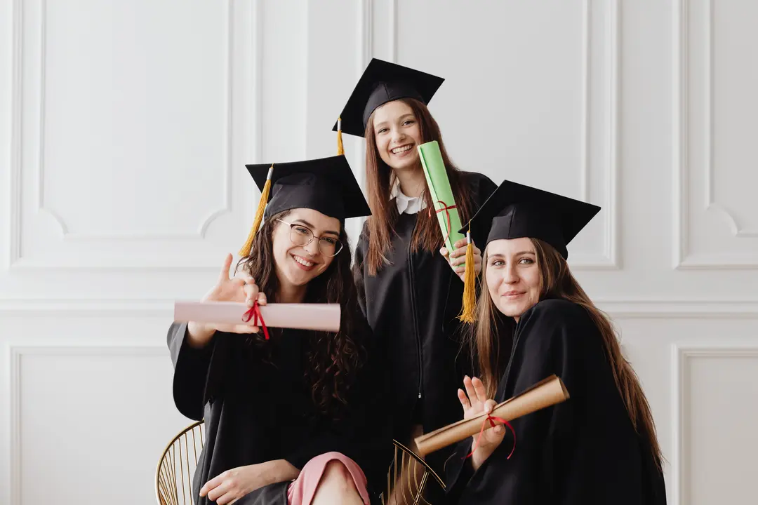 Three graduates holding their degrees to the camera