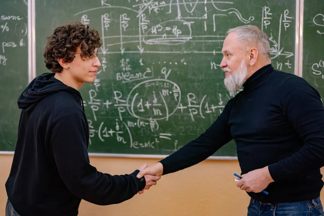 Student and professor shaking hands in front of a chalkboard