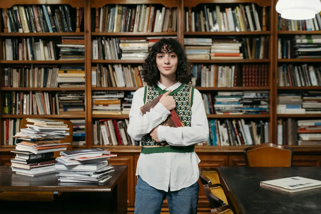 Student holding a book, standing in front of bookshelves